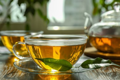 Photo of Fresh green tea in glass cups with saucers, leaves and teapot on table, closeup