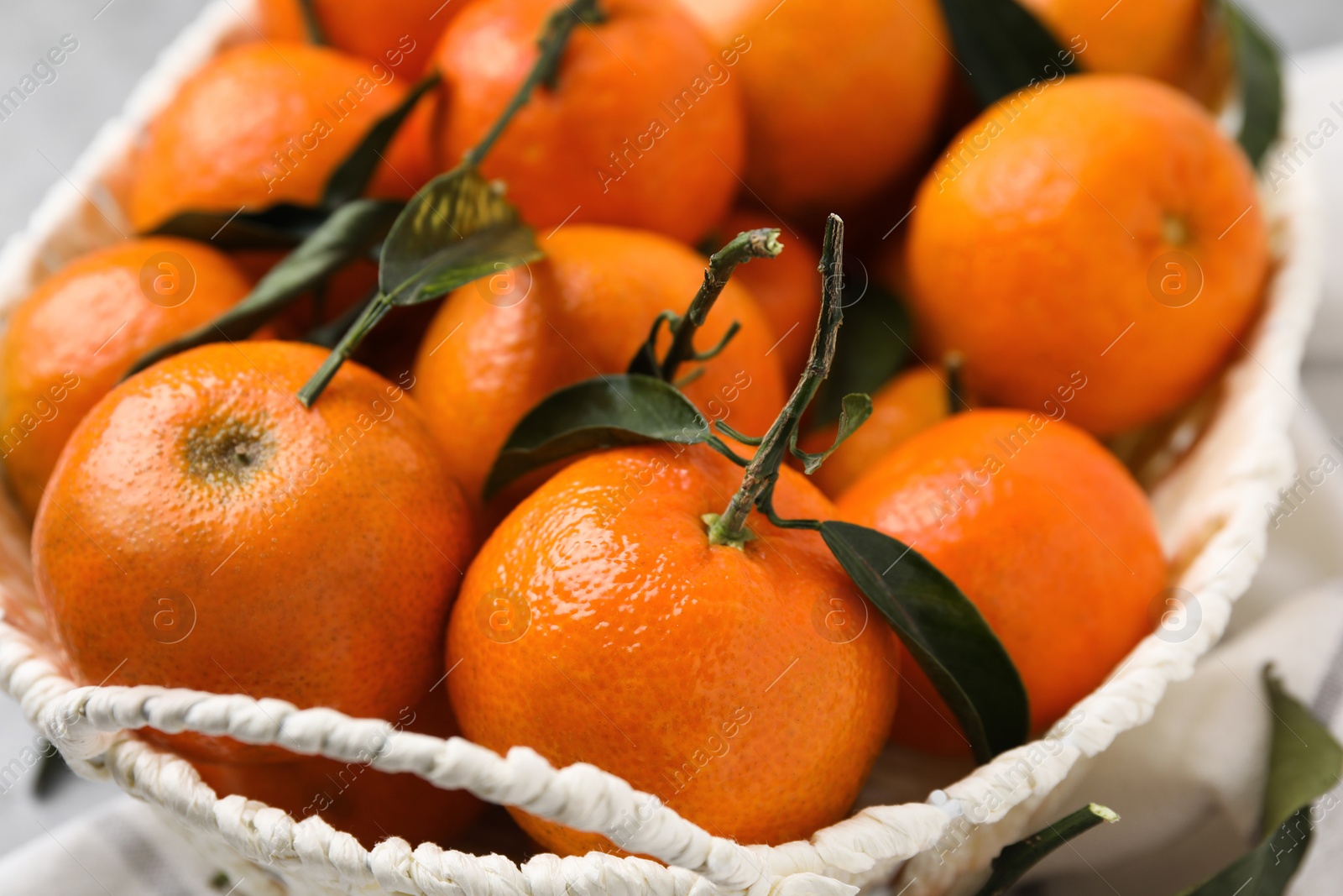 Photo of Fresh ripe tangerines and leaves in basket on table, closeup