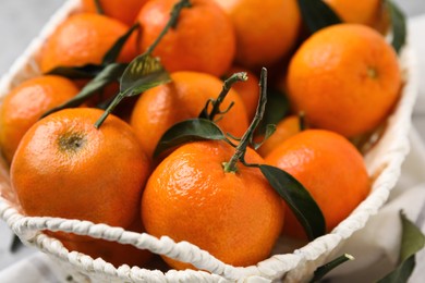 Photo of Fresh ripe tangerines and leaves in basket on table, closeup