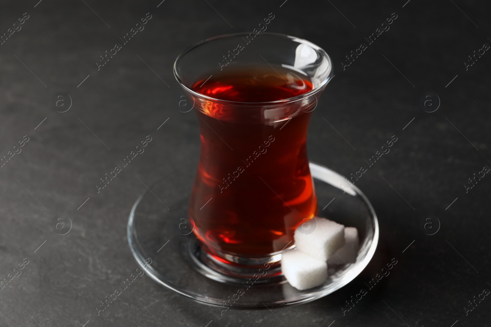 Photo of Glass with traditional Turkish tea and sugar cubes on black table, closeup