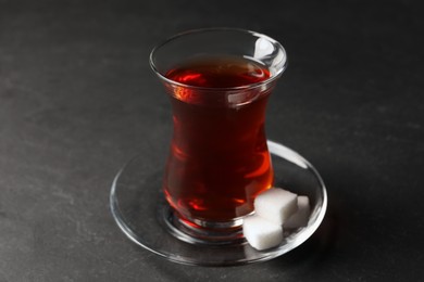Photo of Glass with traditional Turkish tea and sugar cubes on black table, closeup