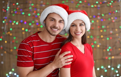 Photo of Young couple in Santa hats on blurred lights background. Christmas celebration