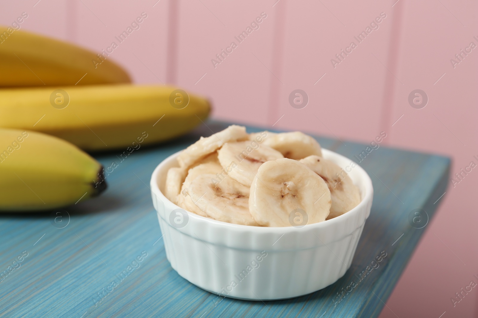 Photo of Bowl with cut bananas near whole fruits on light blue wooden table