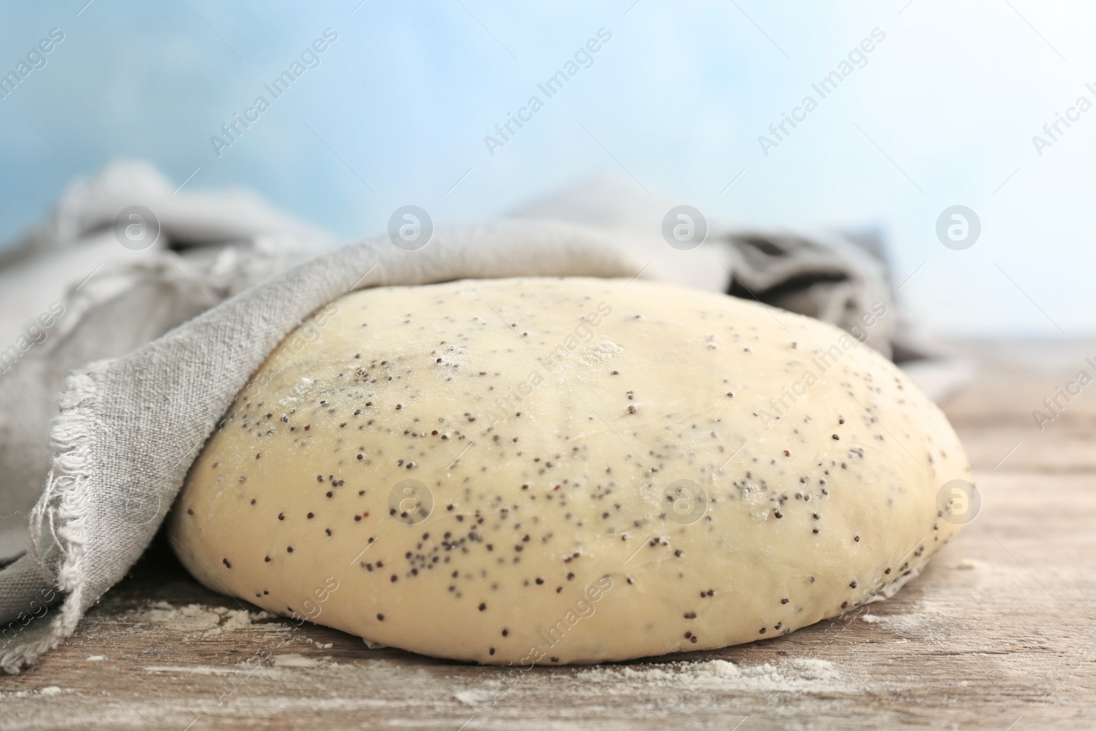 Photo of Raw dough with poppy seeds under towel on wooden table