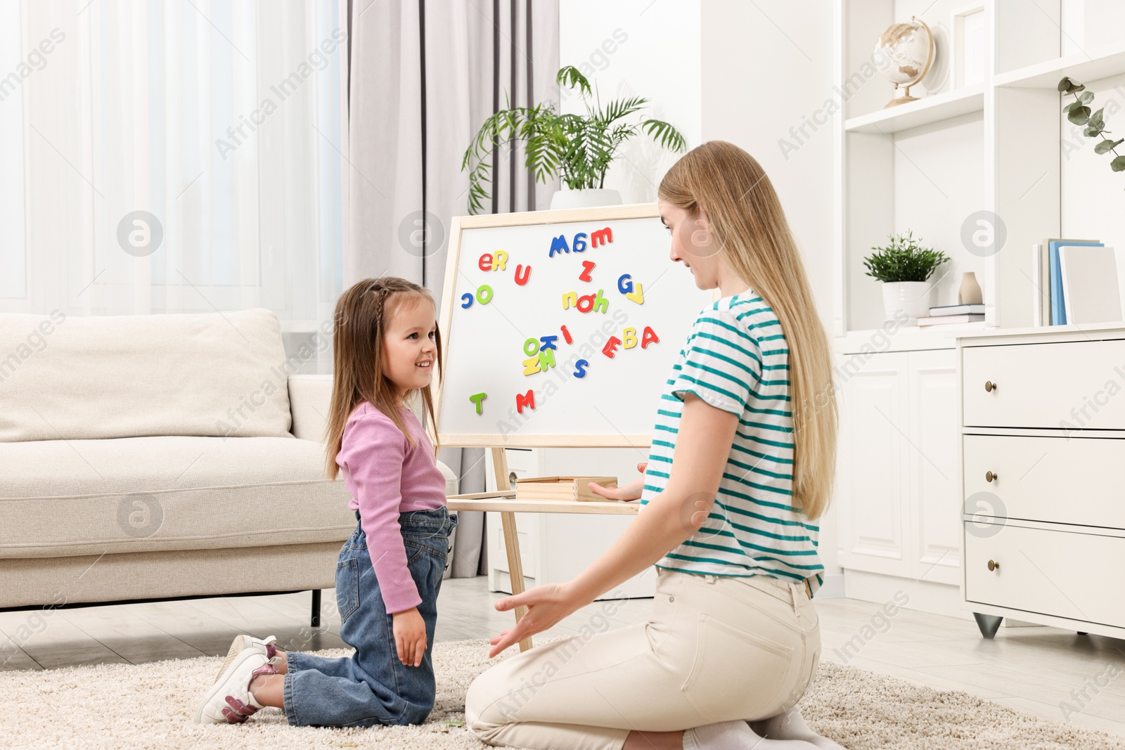 Photo of Mom teaching her daughter alphabet with magnetic letters at home