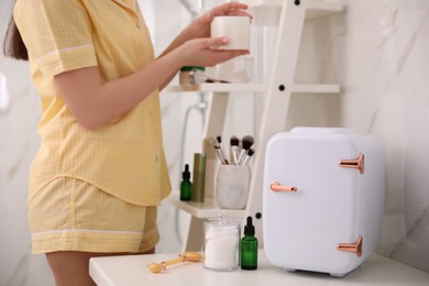 Photo of Woman with cream and cosmetic fridge on counter in bathroom