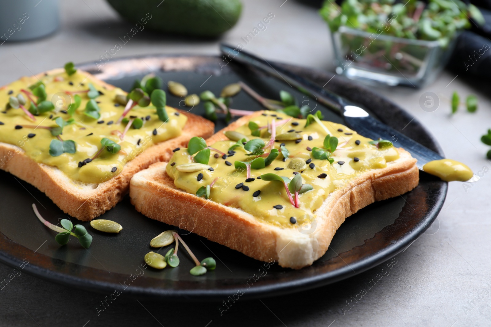 Photo of Delicious sandwiches with guacamole, seeds and microgreens on grey table, closeup