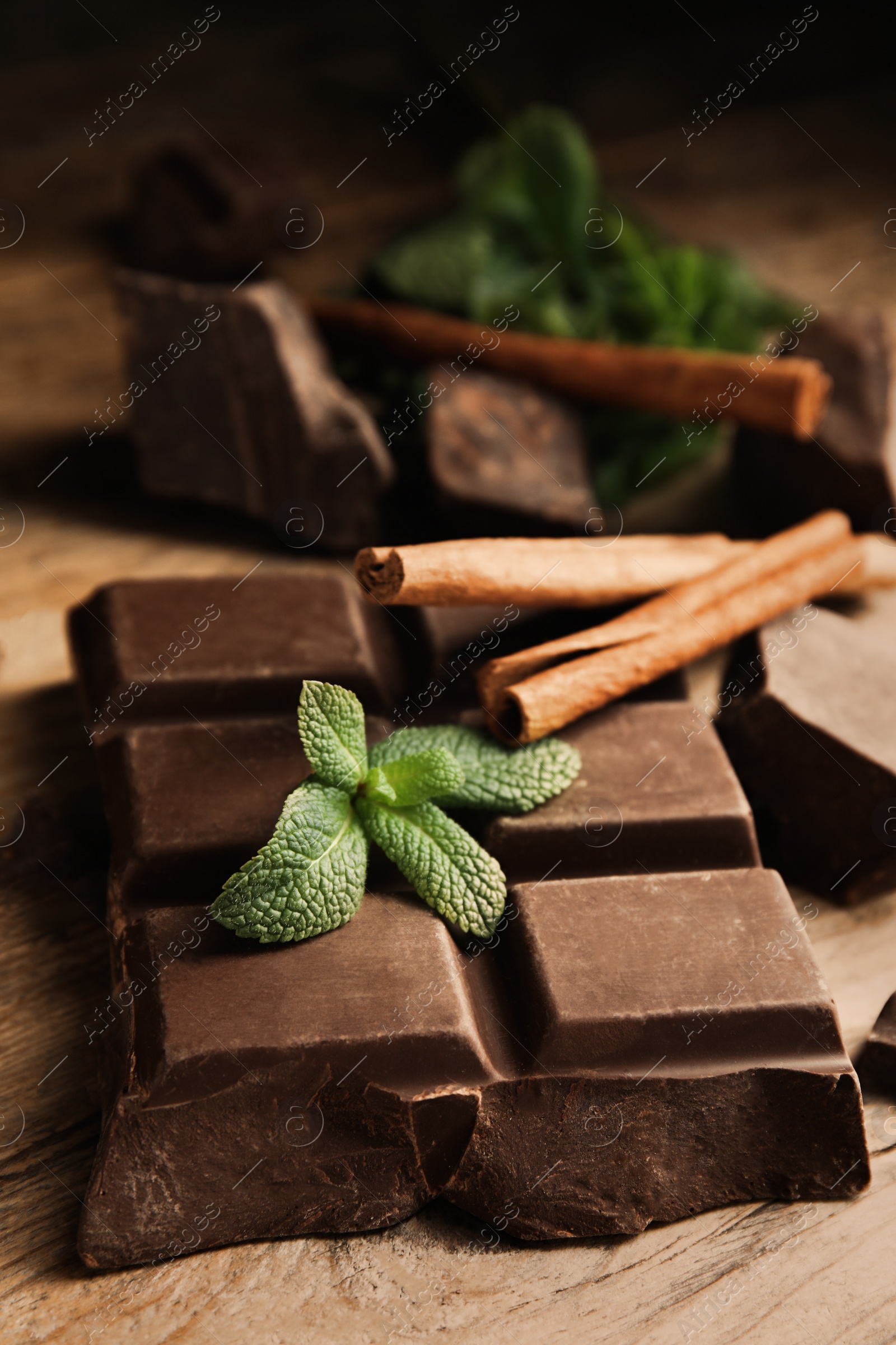 Photo of Tasty chocolate pieces, cinnamon sticks and mint on wooden table, closeup