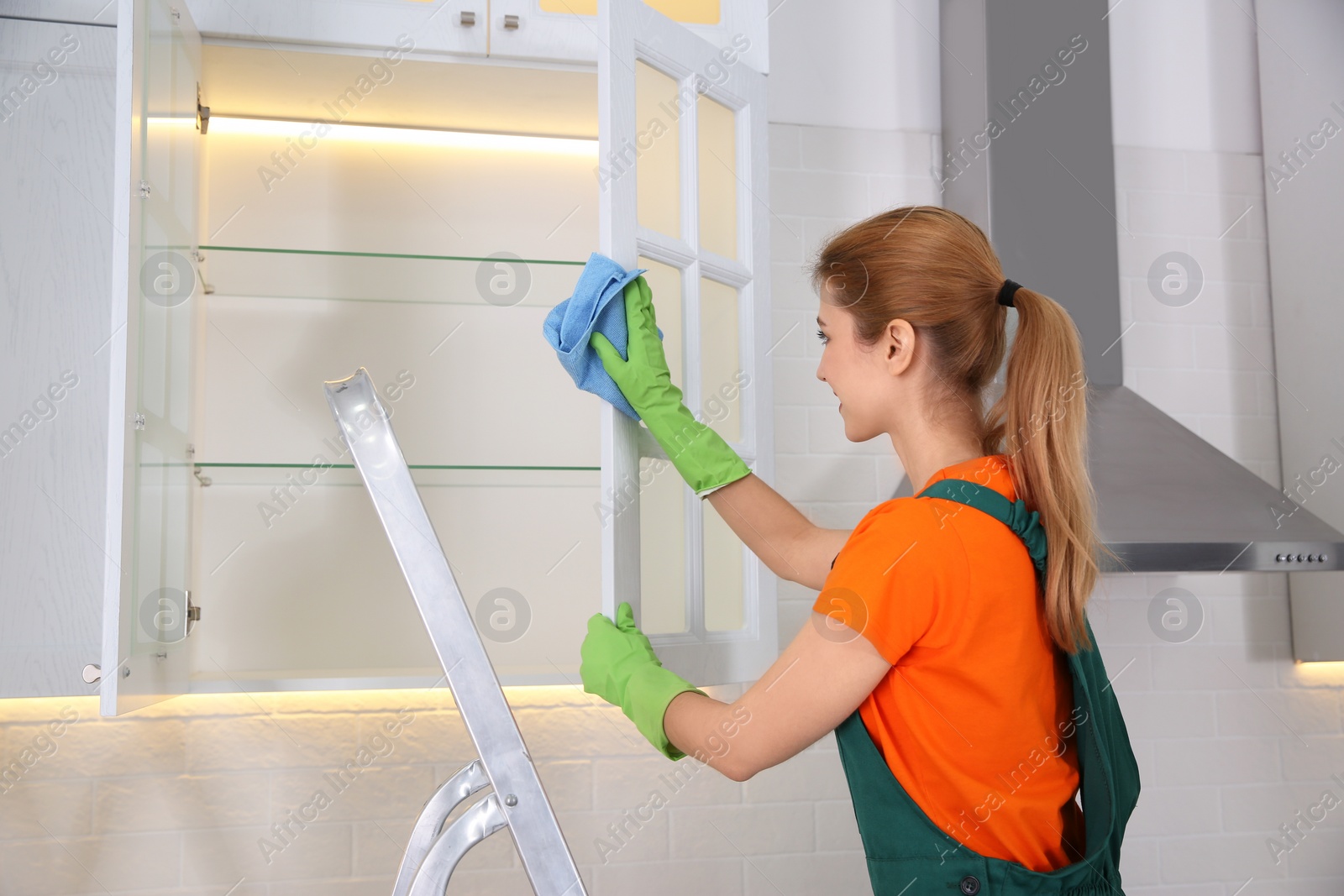 Photo of Professional young janitor cleaning shelves in kitchen