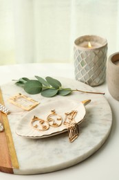 Photo of Stylish golden bijouterie and candle on white table