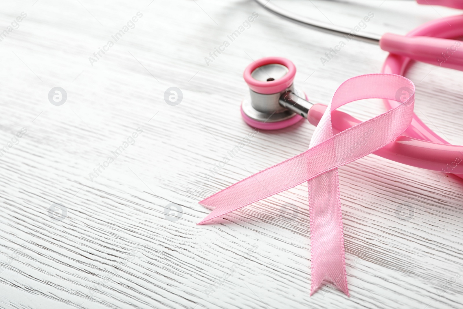 Photo of Pink ribbon and stethoscope on wooden background, space for text. Breast cancer concept