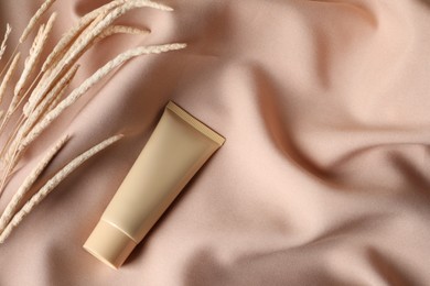 Photo of Tube of skin foundation and decorative plants on beige fabric, flat lay with space for text. Makeup product