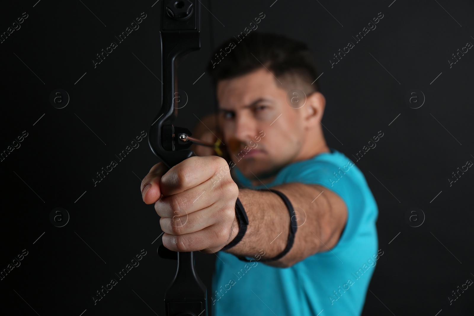 Photo of Man with bow and arrow practicing archery against black background, focus on hand