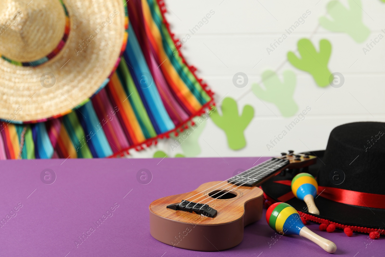 Photo of Black Flamenco hat, ukulele and maracas on purple table. Space for text