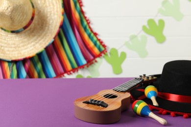 Black Flamenco hat, ukulele and maracas on purple table. Space for text