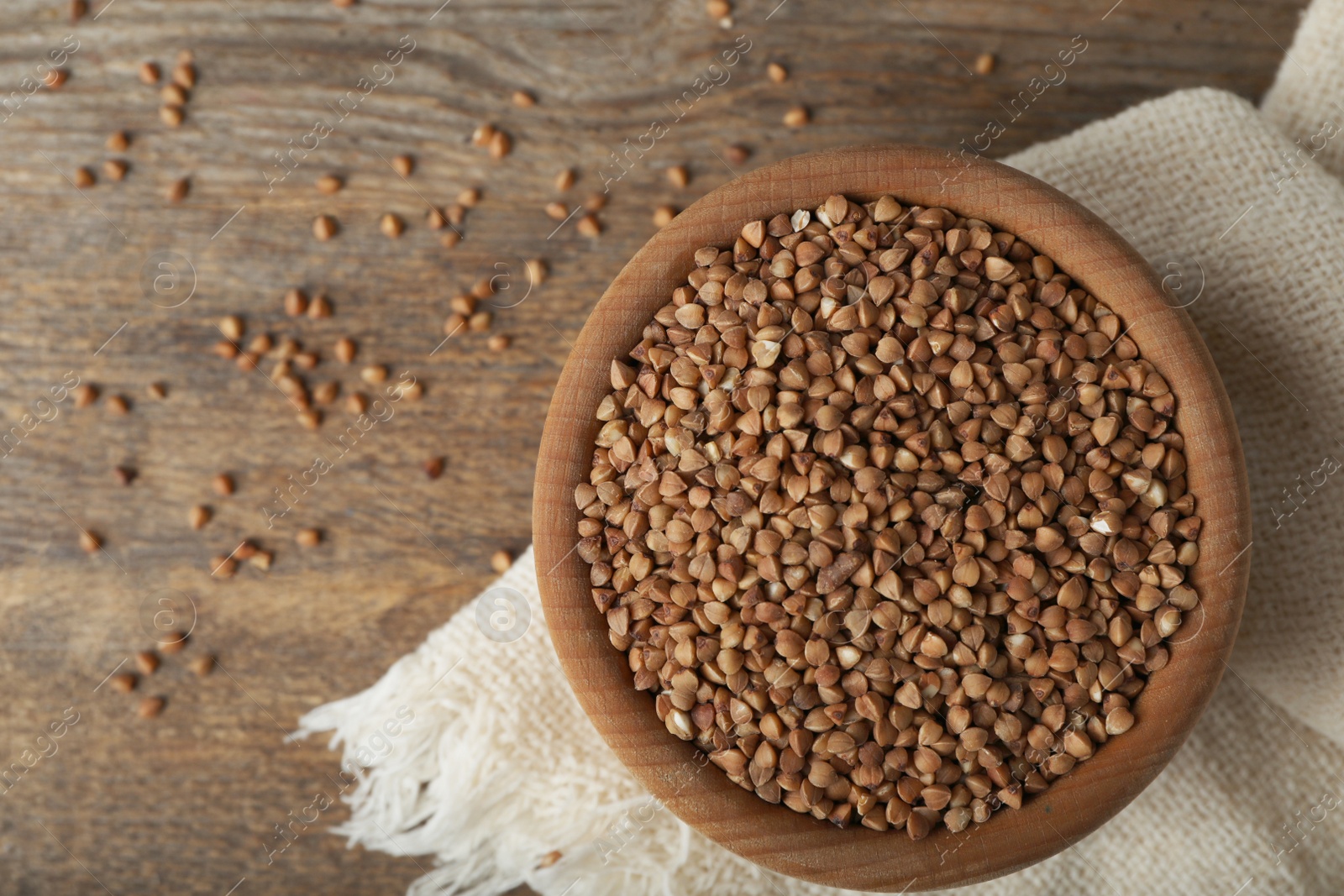 Photo of Uncooked buckwheat in bowl on wooden table, flat lay. Space for text