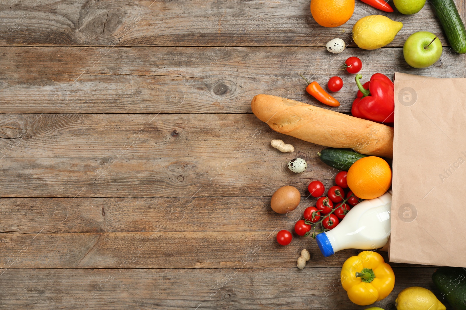 Photo of Flat lay composition with overturned paper bag and groceries on wooden table. Space for text