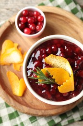 Photo of Cranberry sauce in bowl, fresh berries, rosemary and orange peels on table, top view