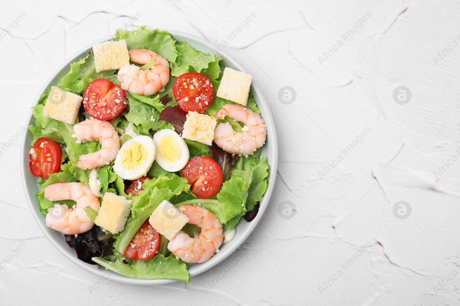 Photo of Delicious Caesar salad with shrimps on white textured table, top view. Space for text