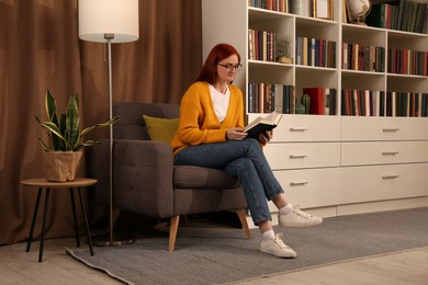 Photo of Beautiful young woman reading book in armchair indoors. Home library