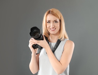 Photo of Young woman with camera against gray background. Professional photo studio