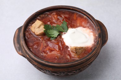 Tasty borscht with sour cream in bowl on light grey table, closeup