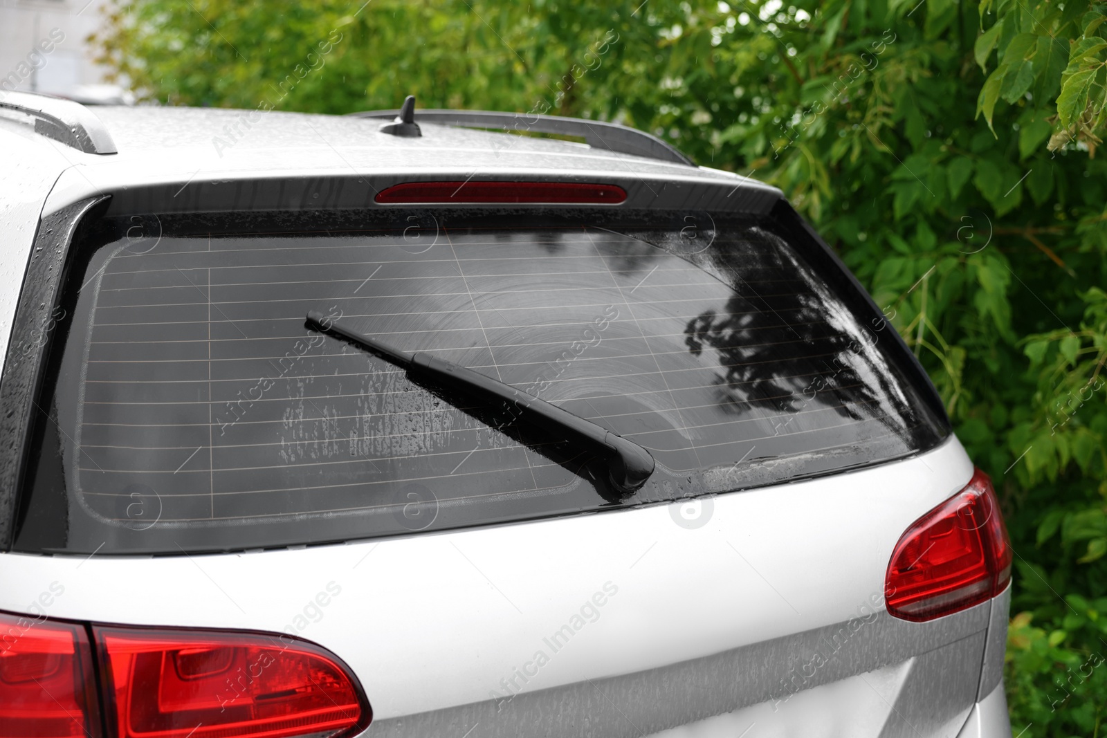 Photo of Wiper cleaning raindrops from car rear windshield outdoors