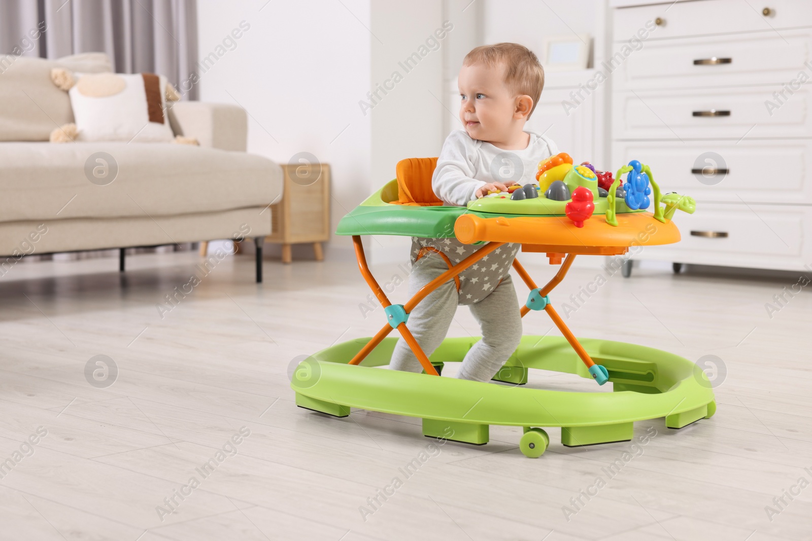 Photo of Cute little boy making first steps with baby walker at home, space for text