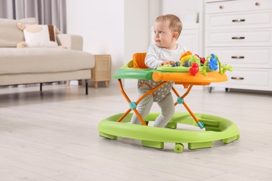 Cute little boy making first steps with baby walker at home, space for text