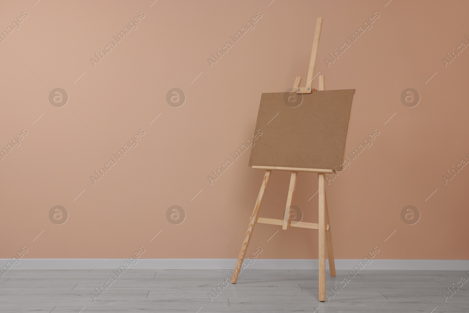 Photo of Wooden easel with blank board near beige wall indoors. Space for text