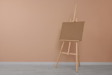 Wooden easel with blank board near beige wall indoors. Space for text