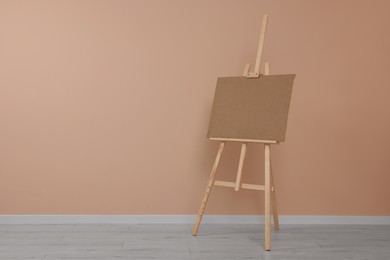 Photo of Wooden easel with blank board near beige wall indoors. Space for text