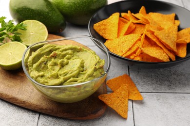 Bowl of delicious guacamole served with nachos chips and lime on white tiled table