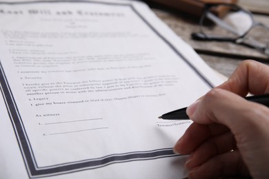 Woman signing last will and testament at table, closeup