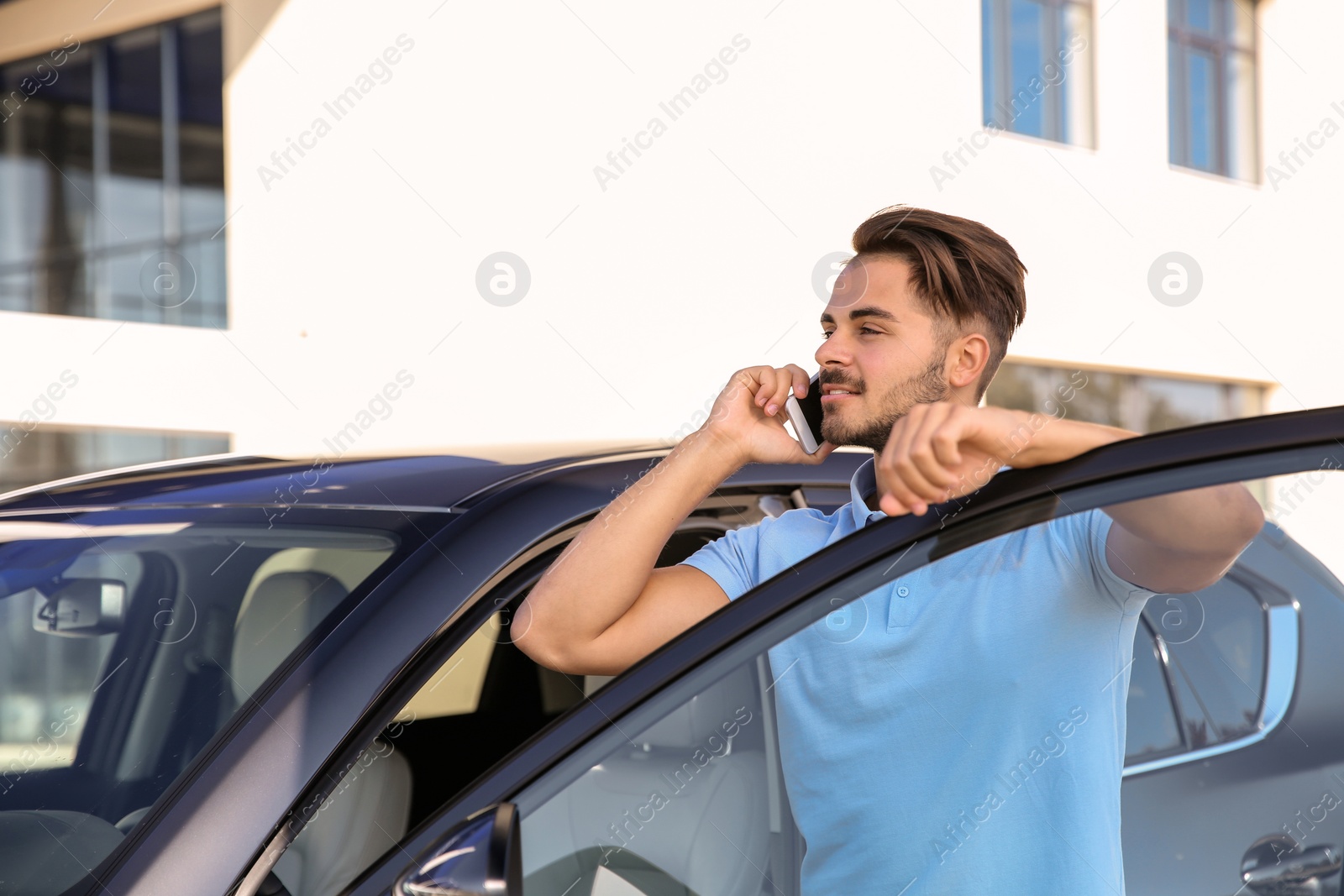 Photo of Young man talking on phone near modern car, outdoors