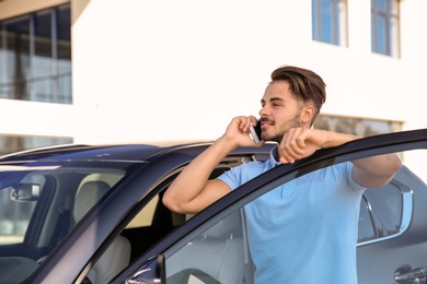 Photo of Young man talking on phone near modern car, outdoors