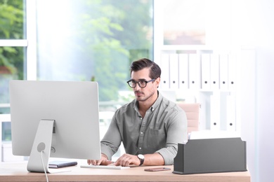 Handsome young man working with computer at table in office