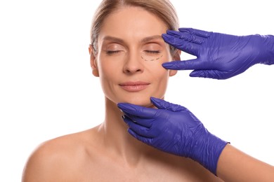 Doctor checking patient's face before cosmetic surgery operation on white background, closeup