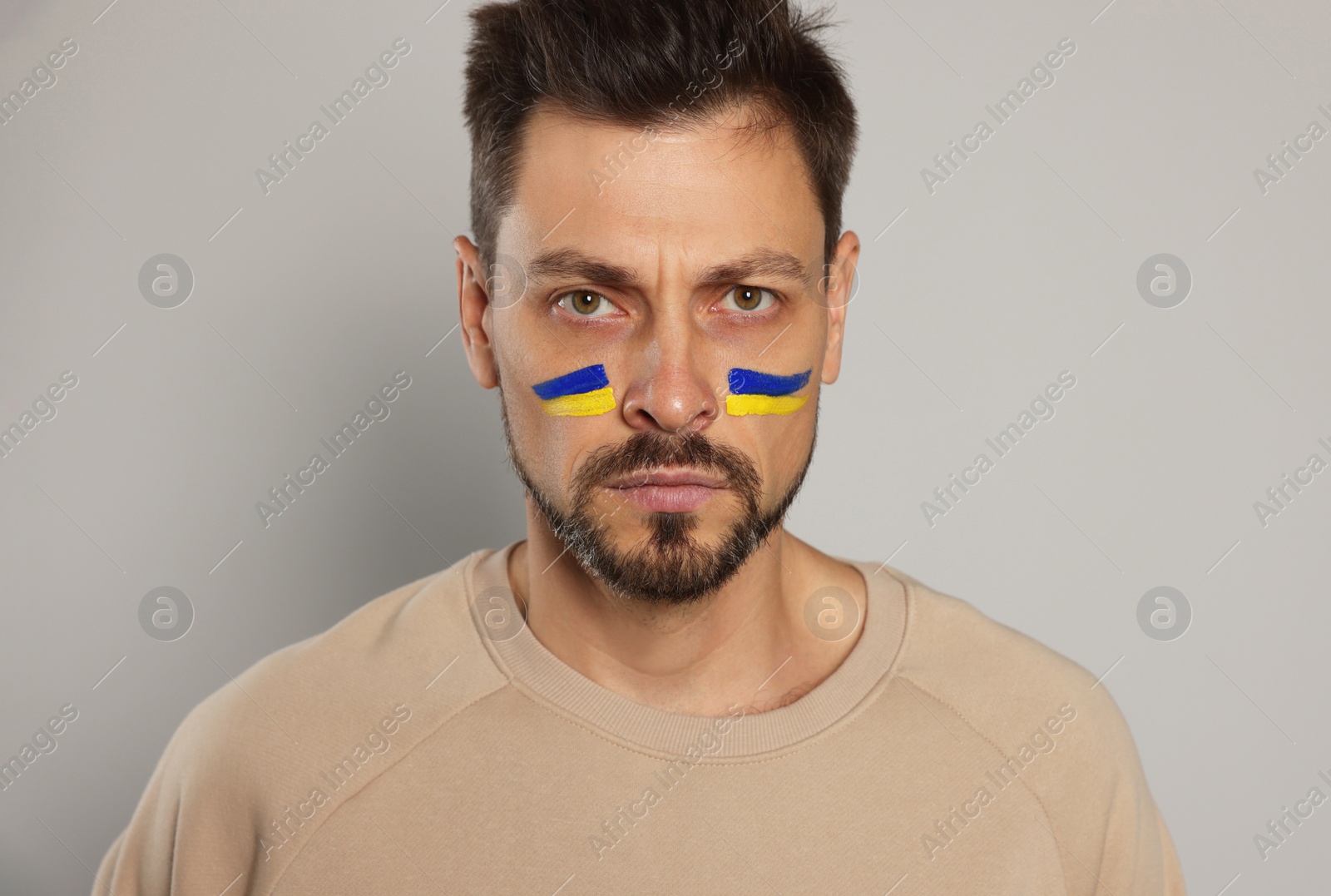 Photo of Angry man with drawings of Ukrainian flag on face against light grey background