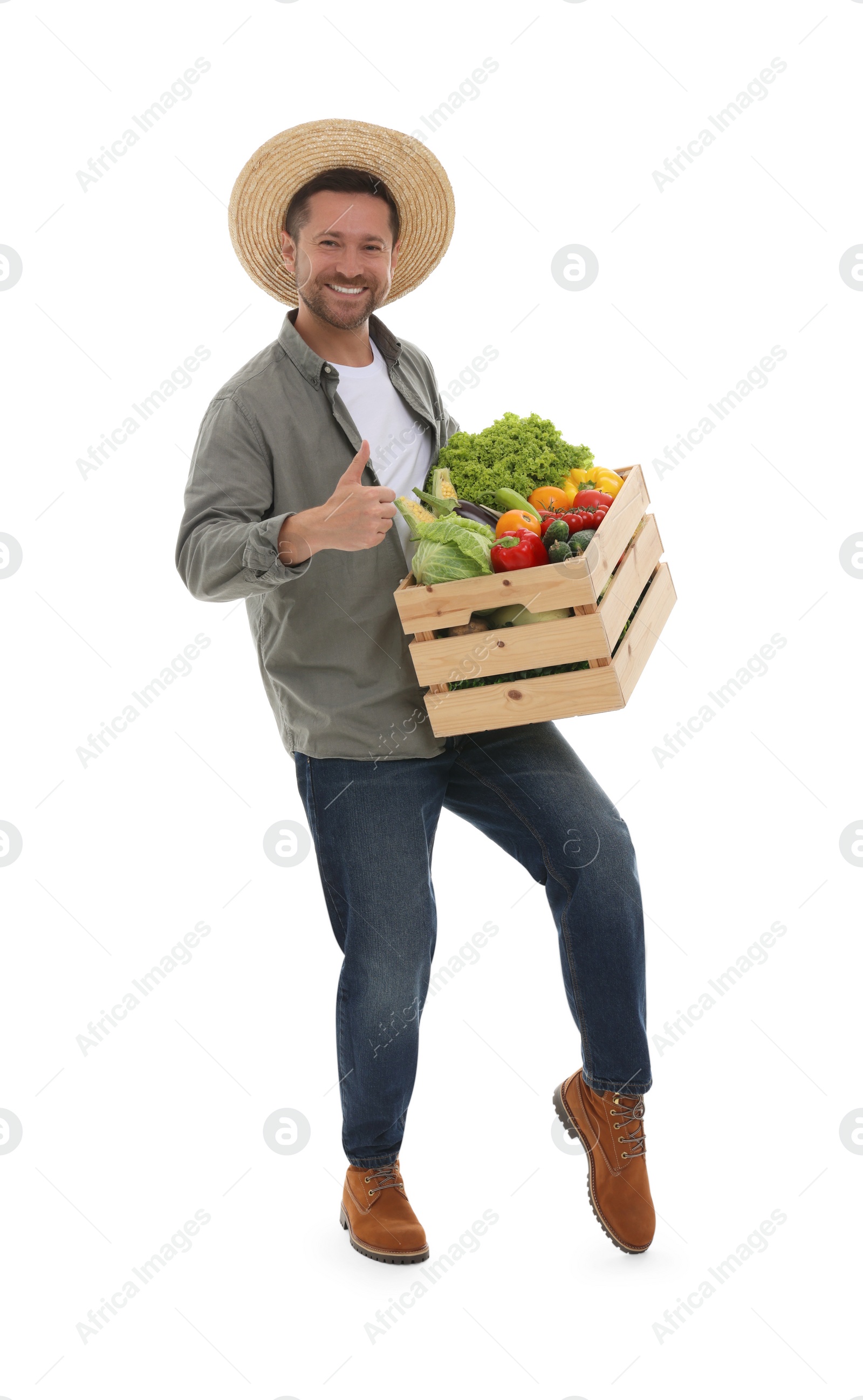 Photo of Harvesting season. Happy farmer holding wooden crate with vegetables and showing thumb up on white background