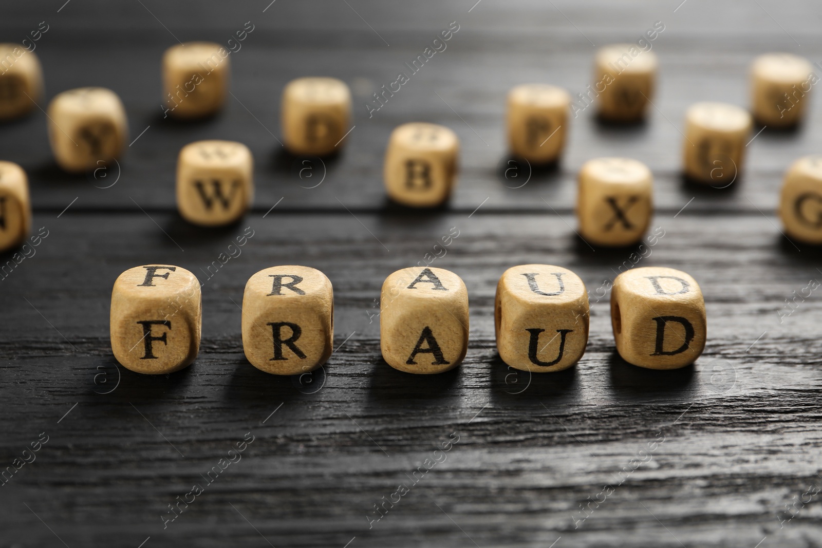 Photo of Word Fraud of cubes with letters on black wooden background