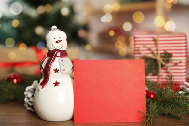 Christmas composition with decorative snowman near red blank card on table, space for text