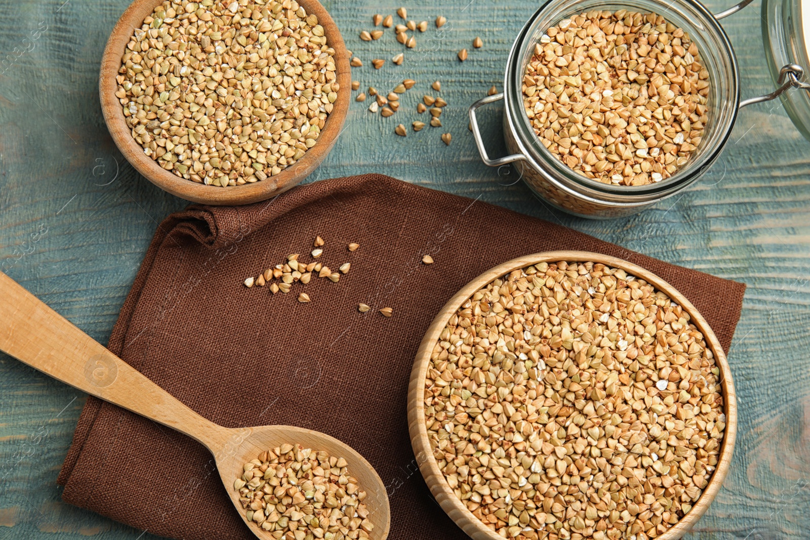 Photo of Uncooked green buckwheat grains on light blue wooden table, flat lay