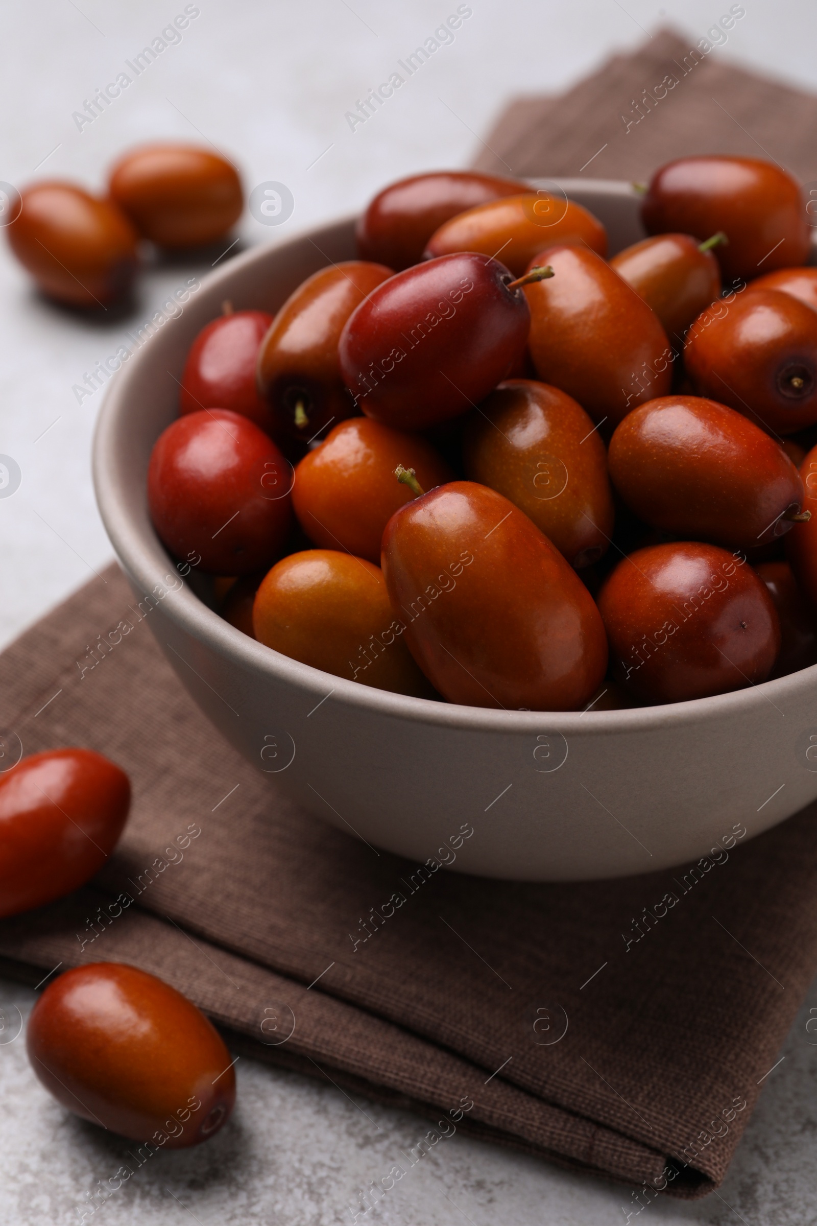 Photo of Fresh Ziziphus jujuba fruits with bowl and napkin on table, closeup