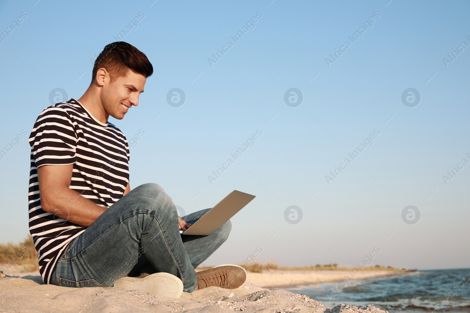 Photo of Man working with laptop on beach. Space for text