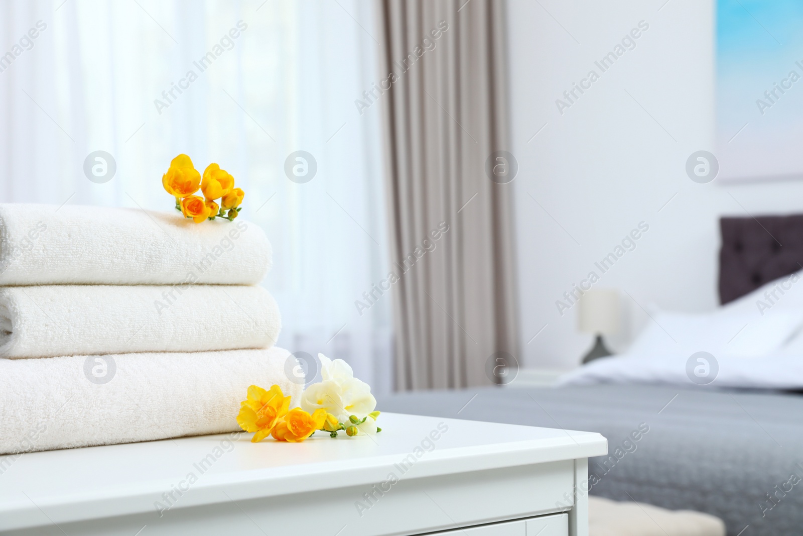 Photo of Stack of fresh towels with flowers on cabinet in bedroom. Space for text