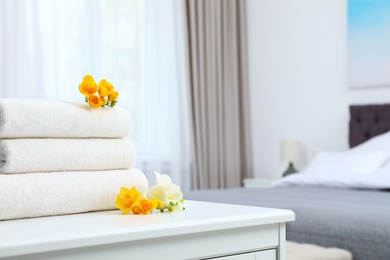 Photo of Stack of fresh towels with flowers on cabinet in bedroom. Space for text