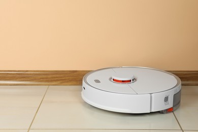 Photo of Robotic vacuum cleaner on white tiled floor near beige wall, space for text
