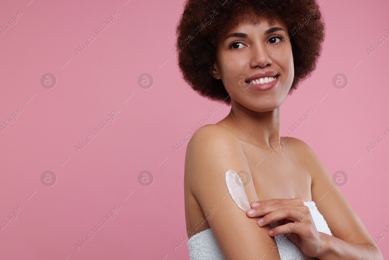 Photo of Beautiful young woman applying body cream onto arm on pink background, space for text