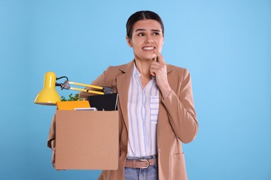 Photo of Thoughtful unemployed woman with box of personal office belongings on light blue background